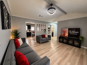 Una sala de estar moderna con un sofá gris, un televisor y una cocina al fondo.