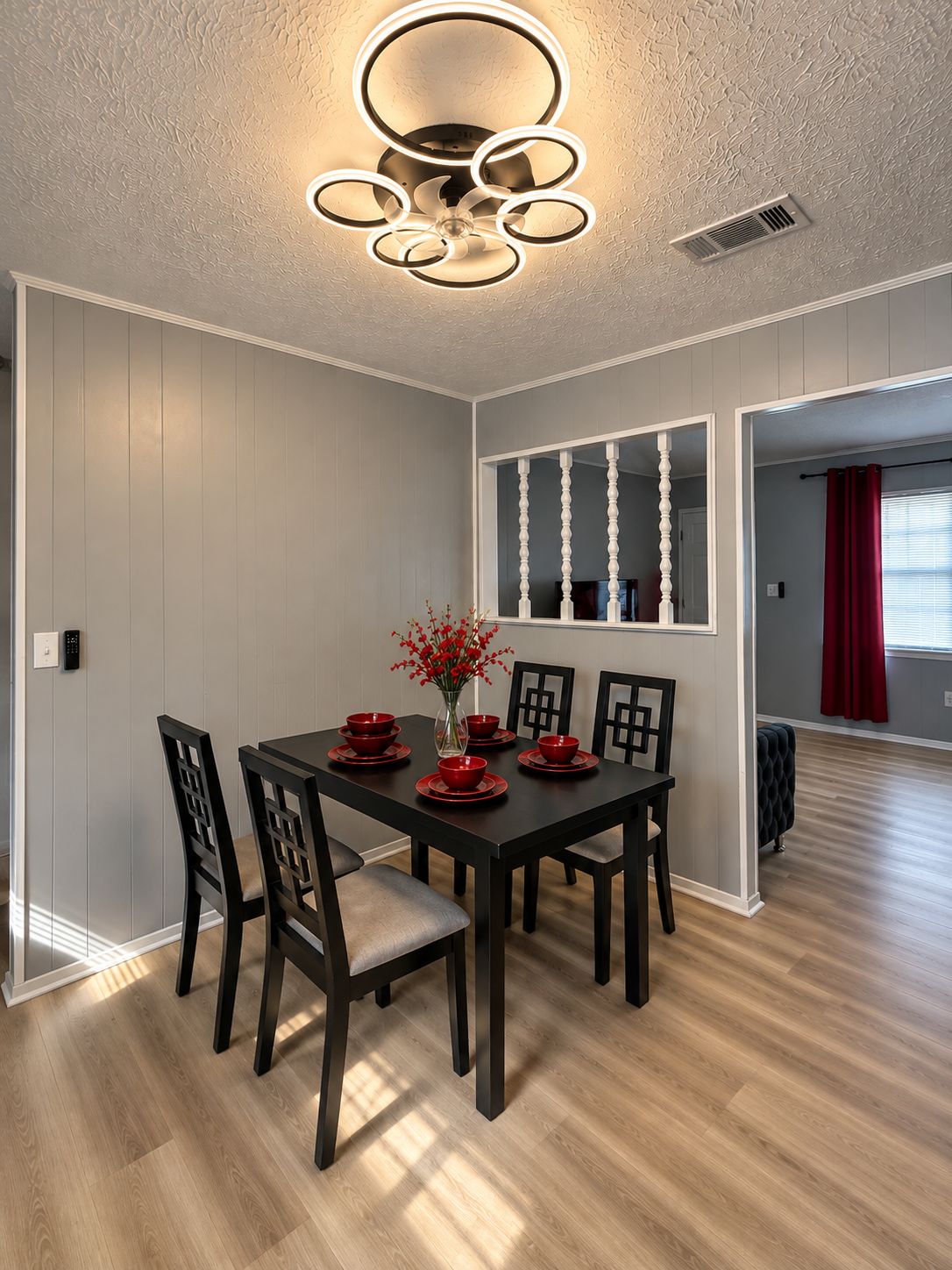 Un coin repas avec une table et des chaises en bois foncé, un vase rempli de fleurs rouges et un luminaire suspendu au plafond.