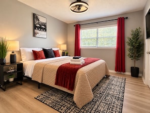 Habitación de hotel con cama, mesita de noche, lámpara, ventana con cortinas y una planta.