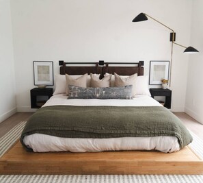 Un dormitorio con una cama plataforma de madera, dos mesitas de noche, un cabecero y dos lámparas de pared.