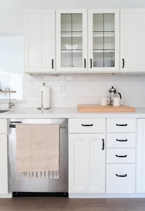 Una cocina con armarios blancos, lavavajillas de acero inoxidable y encimera de madera.