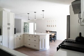 A modern kitchen with white cabinetry, a central island, pendant lighting, and a dining area with a table and chairs.