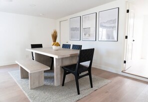 A dining area with a wooden table, black chairs, and a bench. There are framed pictures on the wall.
