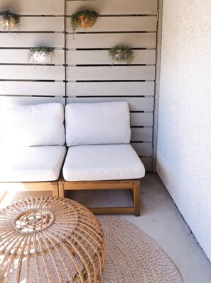 A corner seating area with a wooden bench and cushions, a woven rattan ottoman, and a wall-mounted planter with greenery.