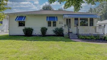 A single-story house with a front porch, two windows with blue awnings, and a small front yard.