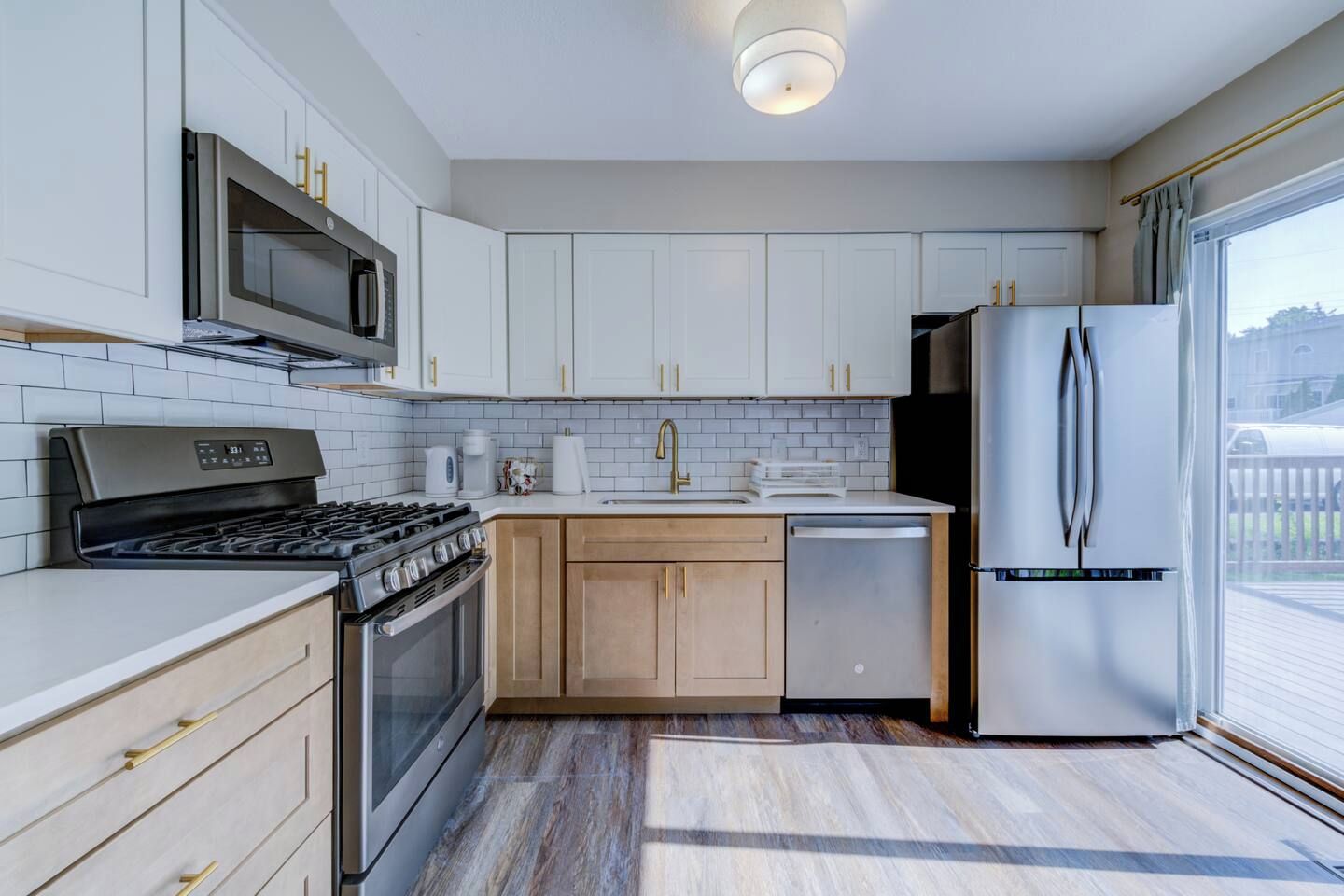Una cocina moderna con armarios blancos, electrodomésticos de acero inoxidable y un amplio ventanal.