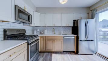 Una cocina moderna con armarios blancos, electrodomésticos de acero inoxidable y un amplio ventanal.
