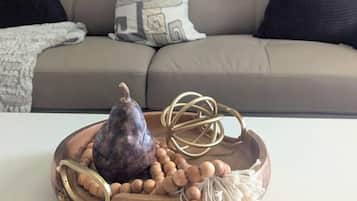 A living room with a sofa, a decorative tray with a fruit, a macrame piece, and a wall painting.