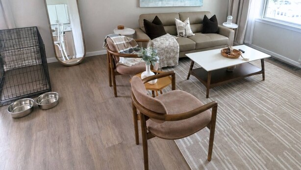 Een woonkamer met een bank, fauteuils, een salontafel, een bijzettafeltje met een vaas, en een spiegel.