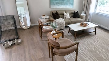 A living room with a sofa, armchairs, a coffee table, a small table with a vase, and a mirror.