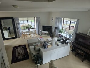 A spacious living room with a white sofa, a coffee table, a TV, and a piano. - Welcome to La Maison Leura, a beautiful 3-bedroom garden retreat in the village. (Leura)