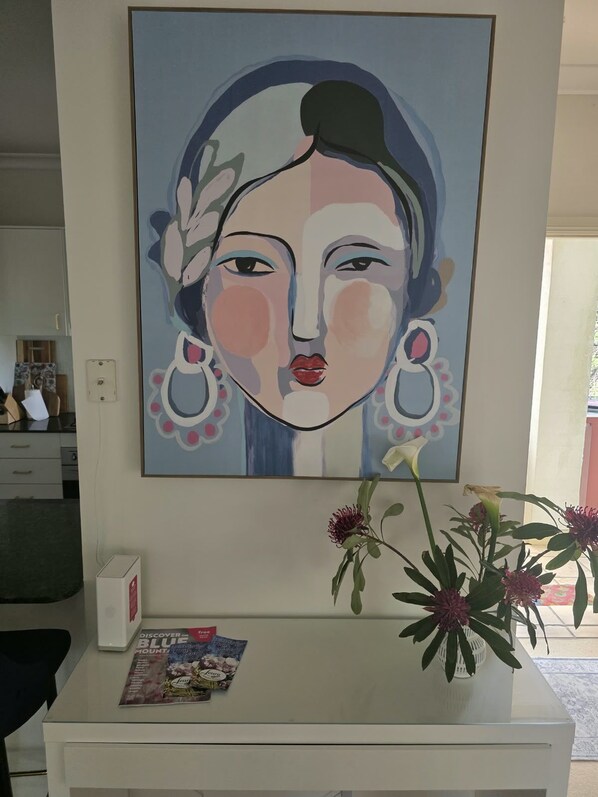 A painting of a woman with floral elements, a white table with a magazine, and a vase with flowers. - Welcome to La Maison Leura, a beautiful 3-bedroom garden retreat in the village. (Leura)