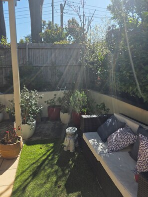 A sunlit patio area with a seating arrangement, potted plants, and a wooden fence. - Welcome to La Maison Leura, a beautiful 3-bedroom garden retreat in the village. (Leura)