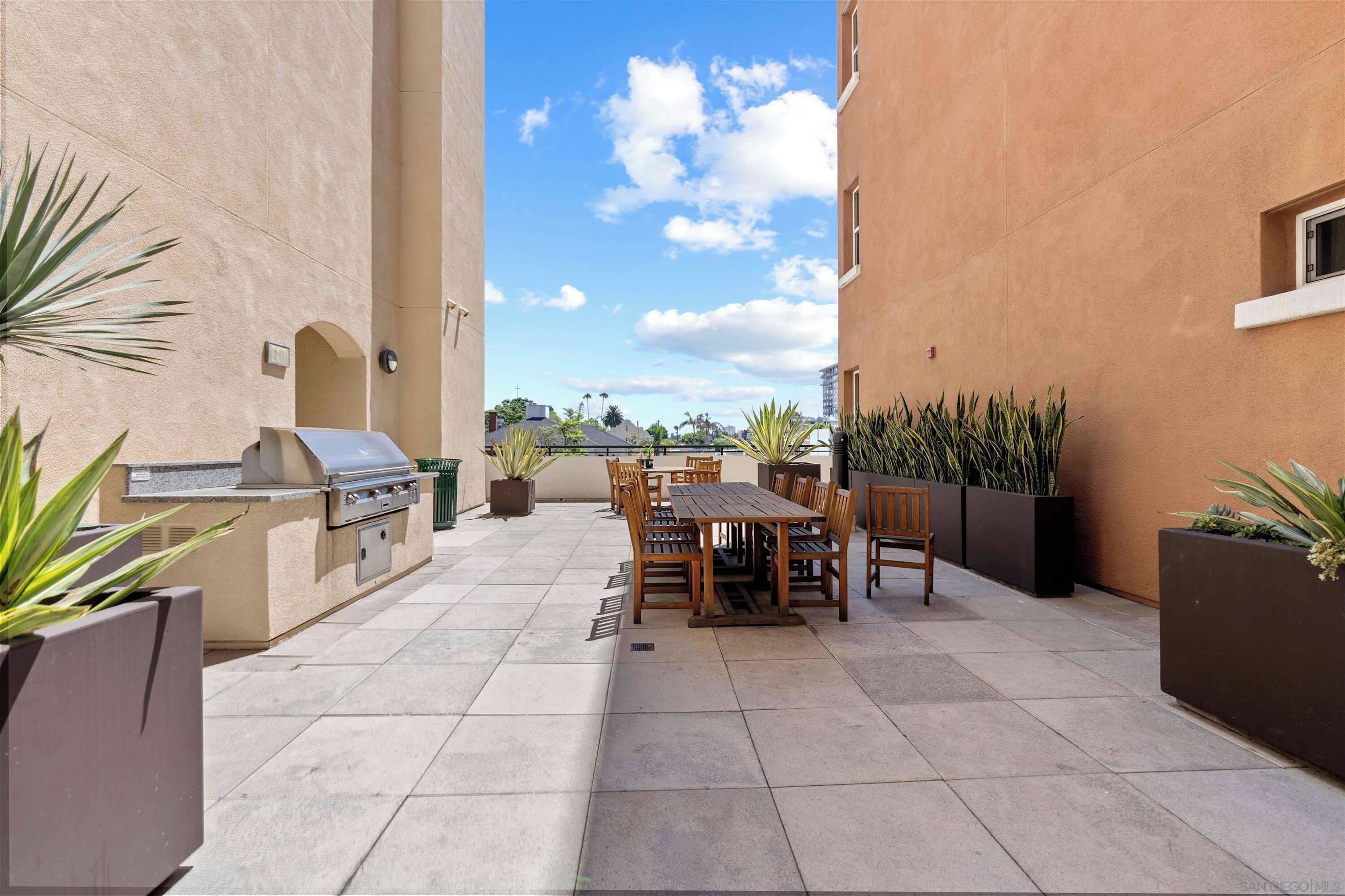 An outdoor patio with a barbecue grill, wooden table and chairs, and potted plants.