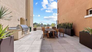 An outdoor patio with a barbecue grill, wooden table and chairs, and potted plants.