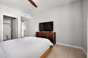 A bedroom with a bed, a television on a wooden cabinet, and a door leading to another room. - The Hudson | Modern Mid-Century Style | City Views (San Diego)