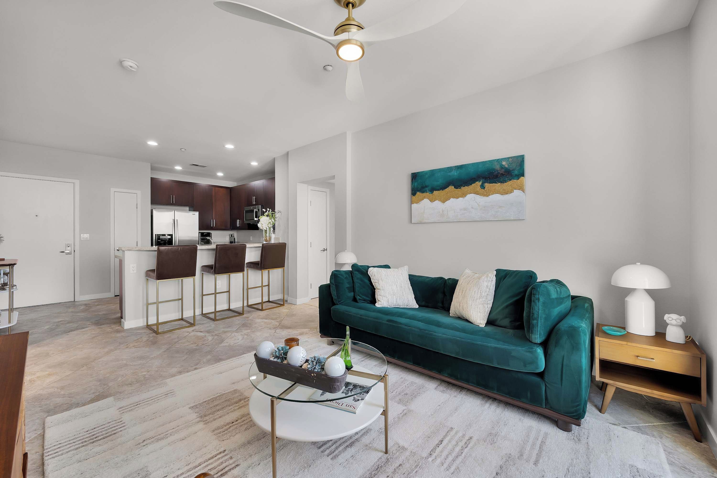 A modern living room with a green sofa, a coffee table, and a dining area with bar stools.