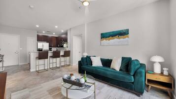 A modern living room with a green sofa, a coffee table, and a dining area with bar stools.