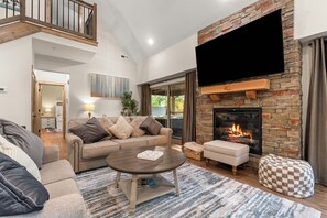 A modern living room with a stone fireplace, a flat-screen TV, a sofa, and a coffee table.
