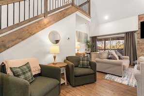 A spacious living area with a staircase, a round mirror, and a view of the outdoors.