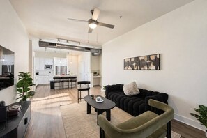A modern living room with a black sofa, a small table, and a ceiling fan. - Spacious & Central 2BD in DT Dallas (Dallas)