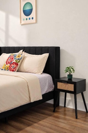 A bedroom with a black headboard, a bed with a floral pillow, a bedside table with a plant, and a wall-mounted abstract art piece. - Spacious & Central 2BD in DT Dallas (Dallas)