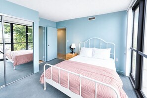 A bedroom with a bed, a nightstand, a mirror, and a window. - Golden Sands 101 (Ocean City)