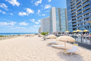 A beach with sun loungers and umbrellas, a boardwalk, and high-rise buildings in the background. - Golden Sands 101 (Ocean City)