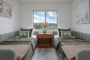 Ein Schlafzimmer mit zwei Betten, einem Fenster mit Ausblick, einer Lampe und Kunstwerken an den Wänden.
