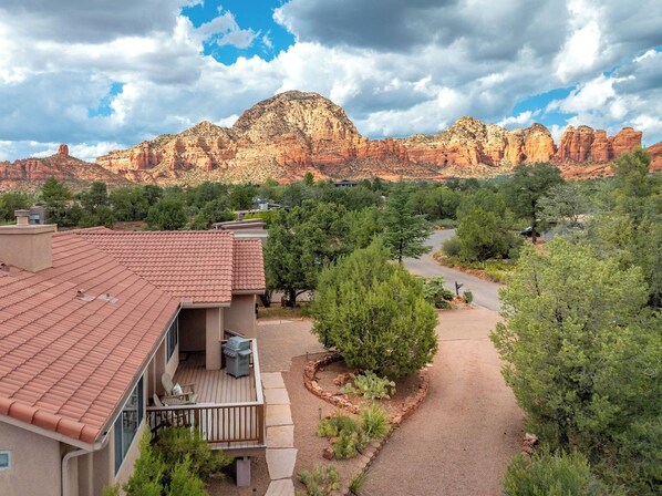 Una zona residenziale con una casa caratterizzata da un tetto in tegole rosse, un patio e un giardino curato con un vialetto che conduce a una vista sulle montagne.