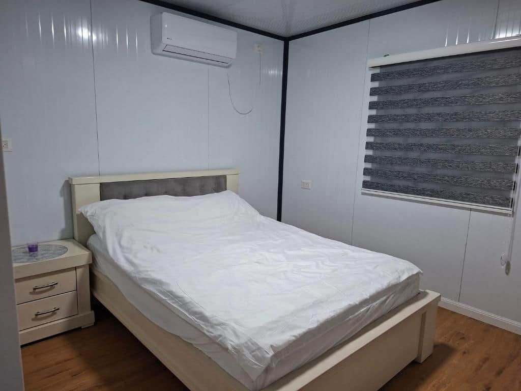 Une chambre à coucher comprenant un lit, une table de chevet, une fenêtre avec des stores et un appareil de climatisation.