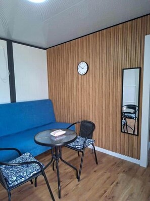 A room with a blue sofa, a round table with two chairs, a wooden wall panel, a clock, and a mirror.