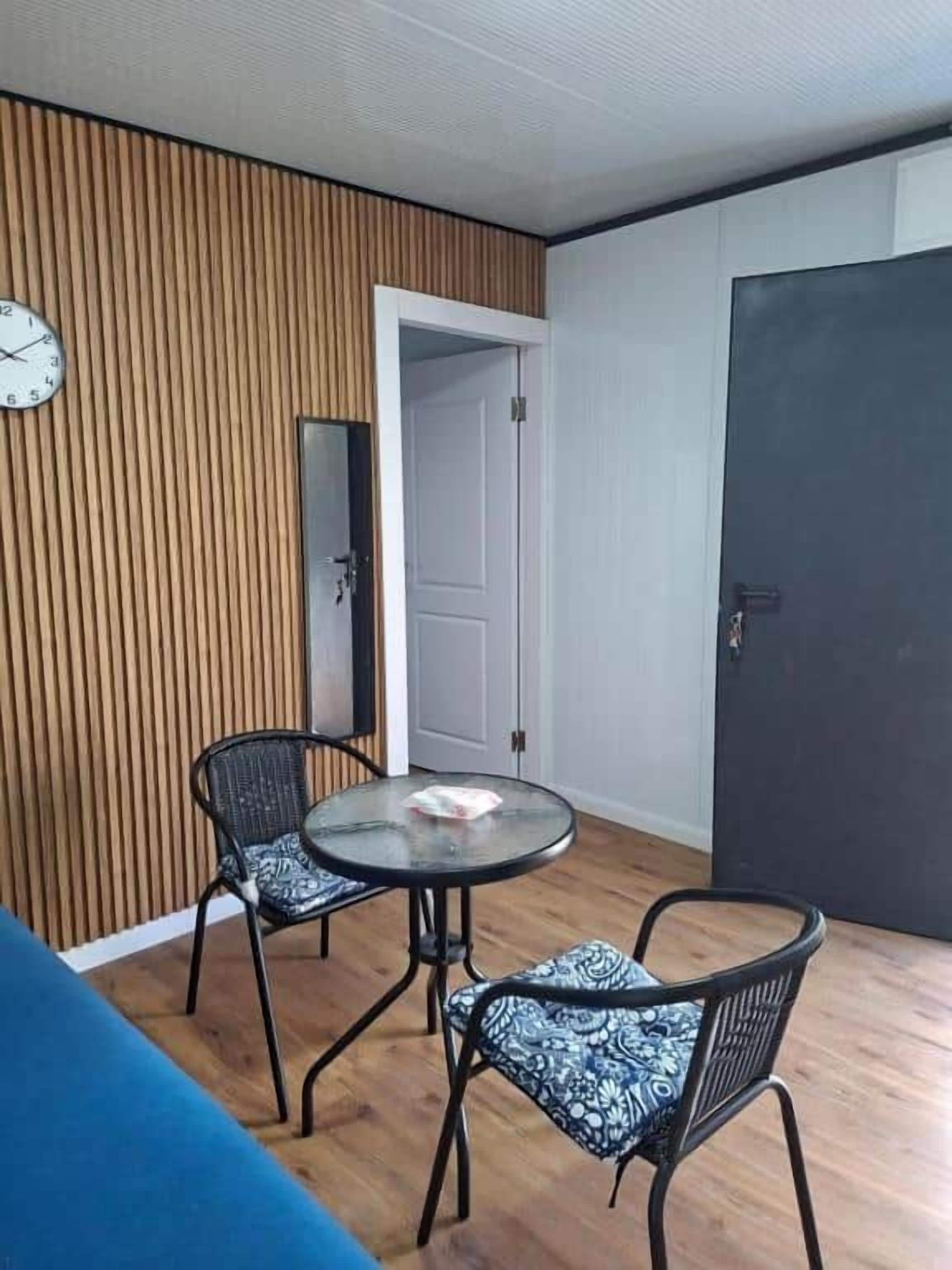 A room with a round table, two chairs, a clock on the wall, and a door.