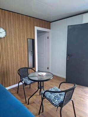 A room with a round table, two chairs, a clock on the wall, and a door.
