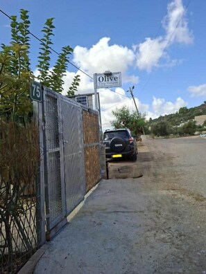 A fenced property with a sign reading 'Olive Tiny House' and a road leading to a parked vehicle.