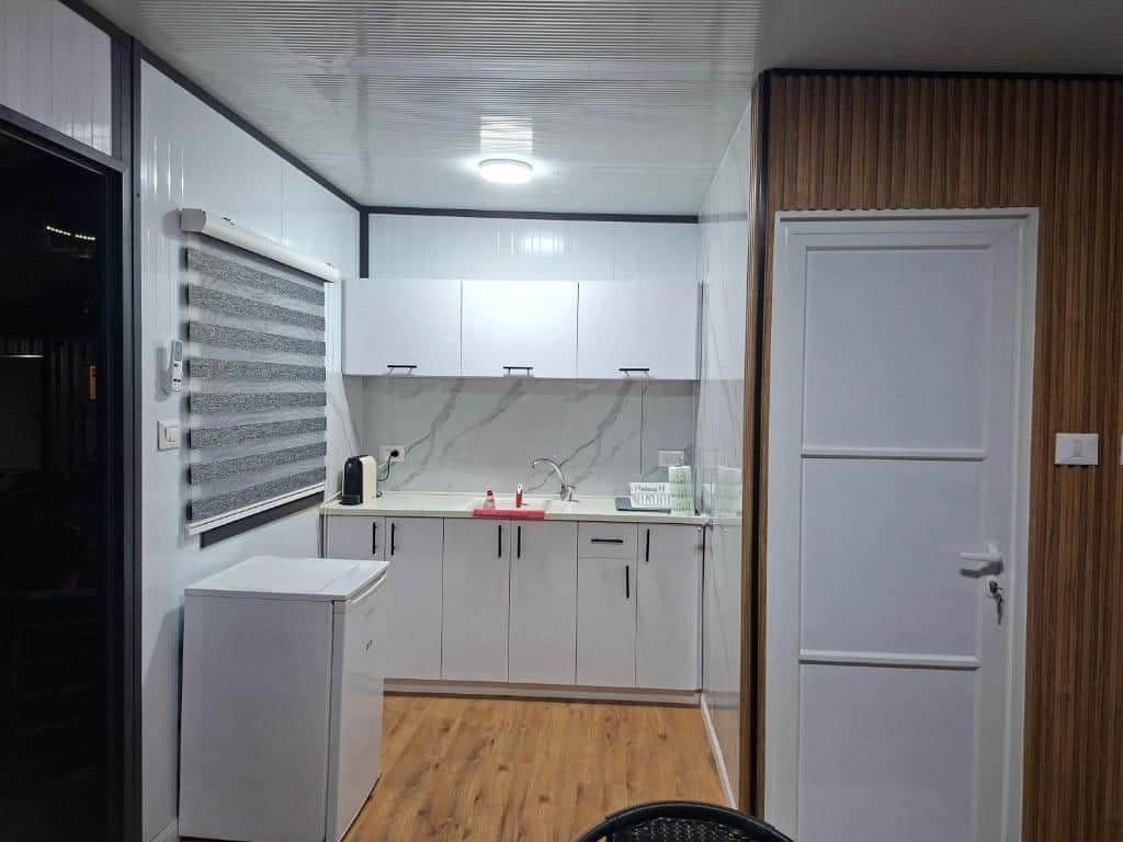 Una cocina compacta con armarios blancos, horno integrado y un refrigerador pequeño.