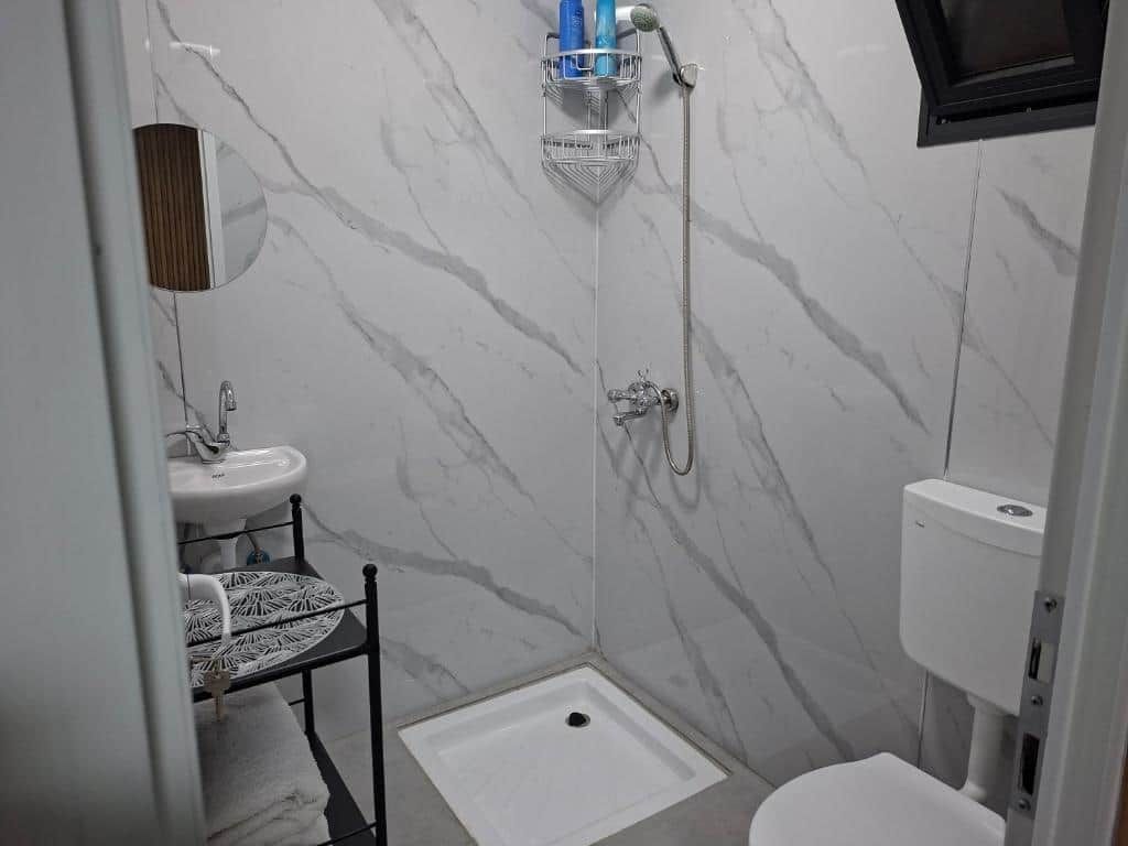 Un baño con ducha, inodoro, lavabo y un taburete pequeño.