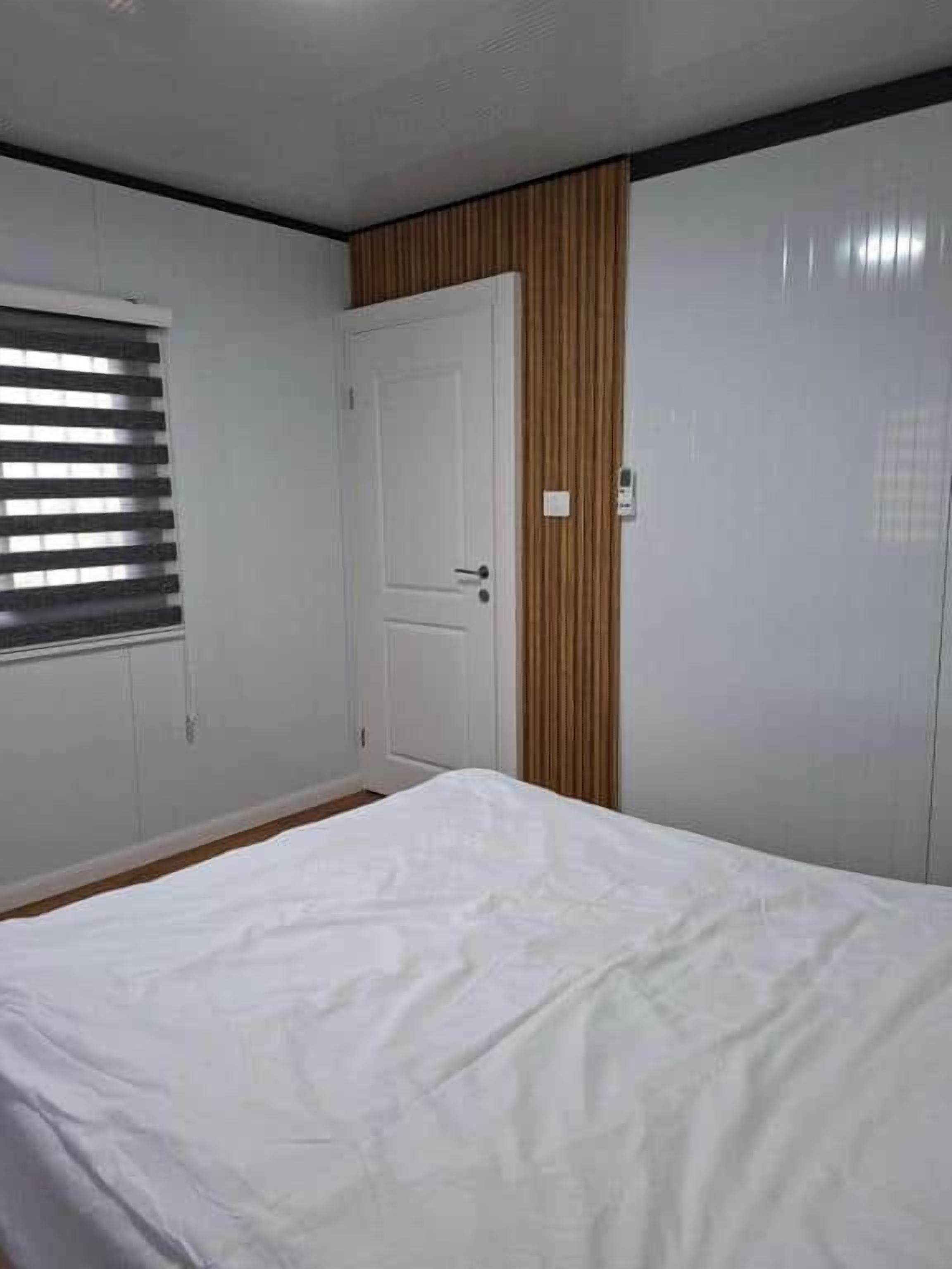 Un dormitorio con cama, puerta y ventana con persianas.