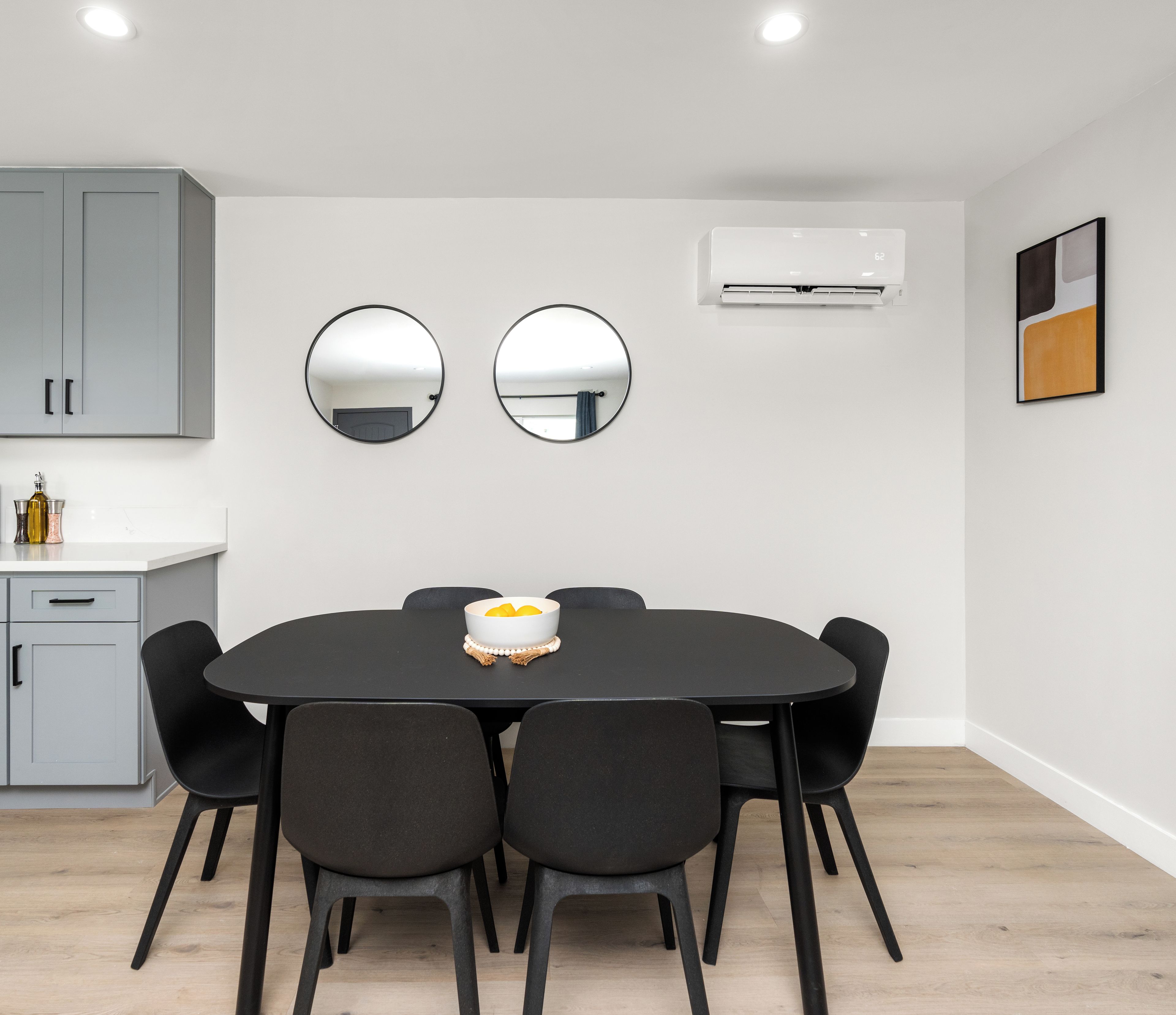 Un espace repas moderne avec une table ronde, six chaises et deux miroirs fixés au mur.
