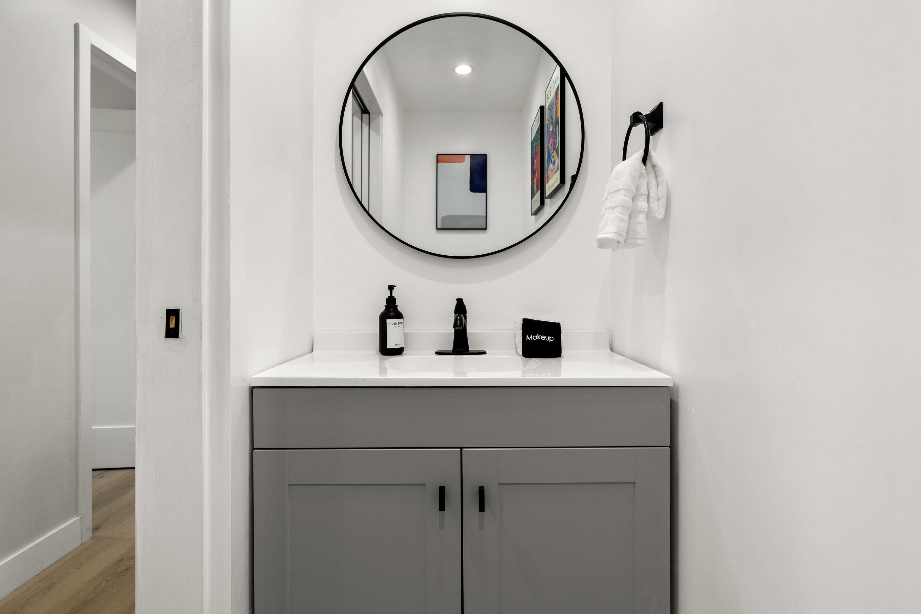Une salle de bain avec un meuble-lavabo blanc, un miroir rond et une serviette accrochée au mur.