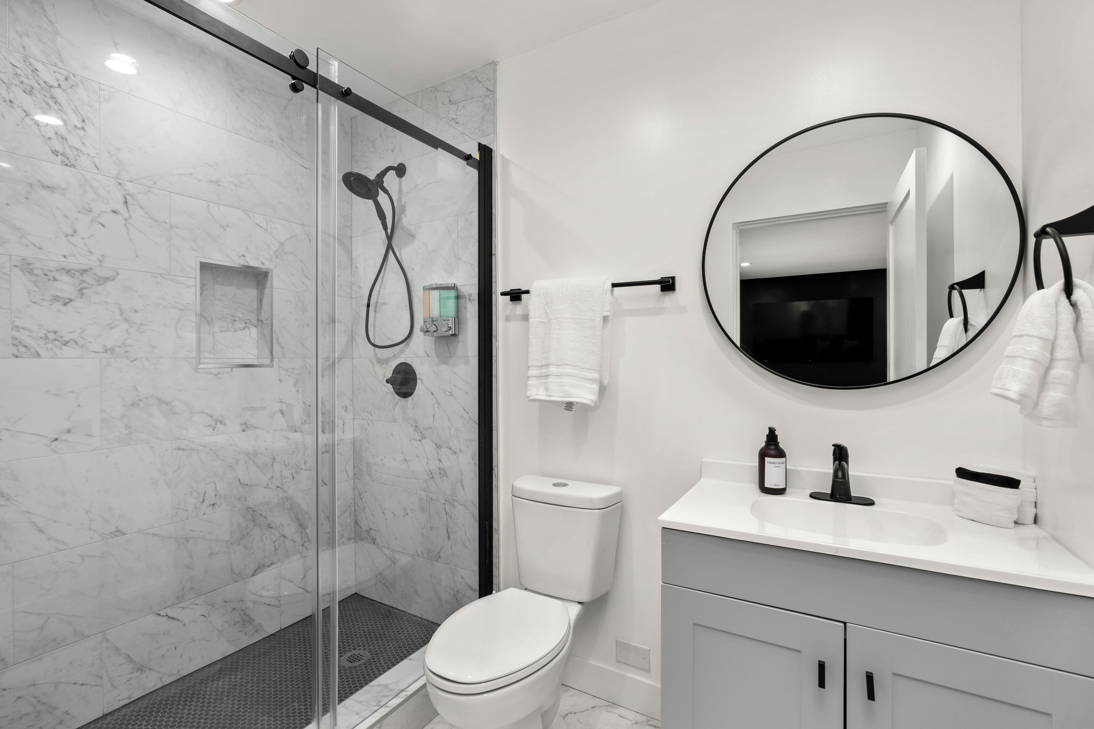 Un bagno moderno con doccia vetro, toilette, lavabo con specchio e porta asciugamani.