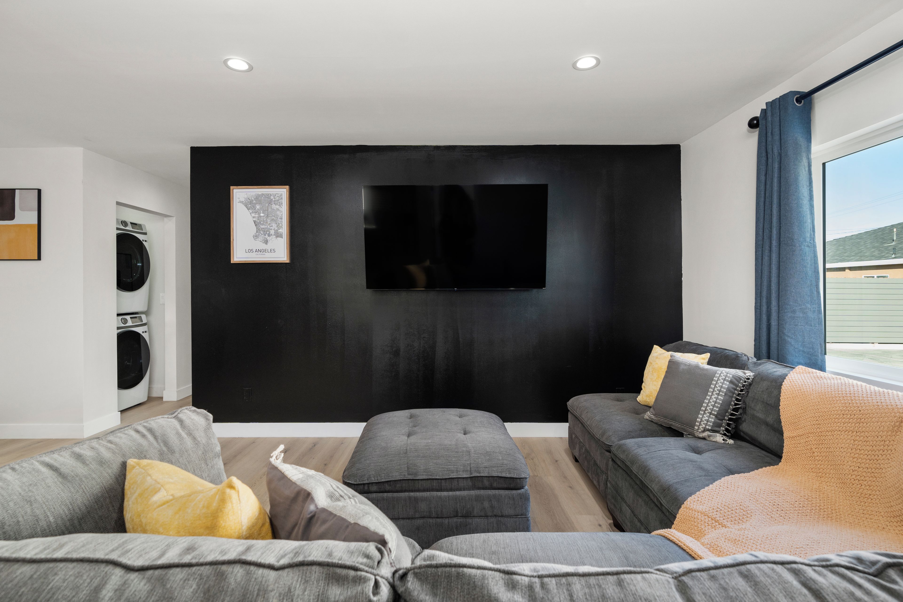 Un salon moderne avec un téléviseur à écran plat, des canapés gris et une grande fenêtre.