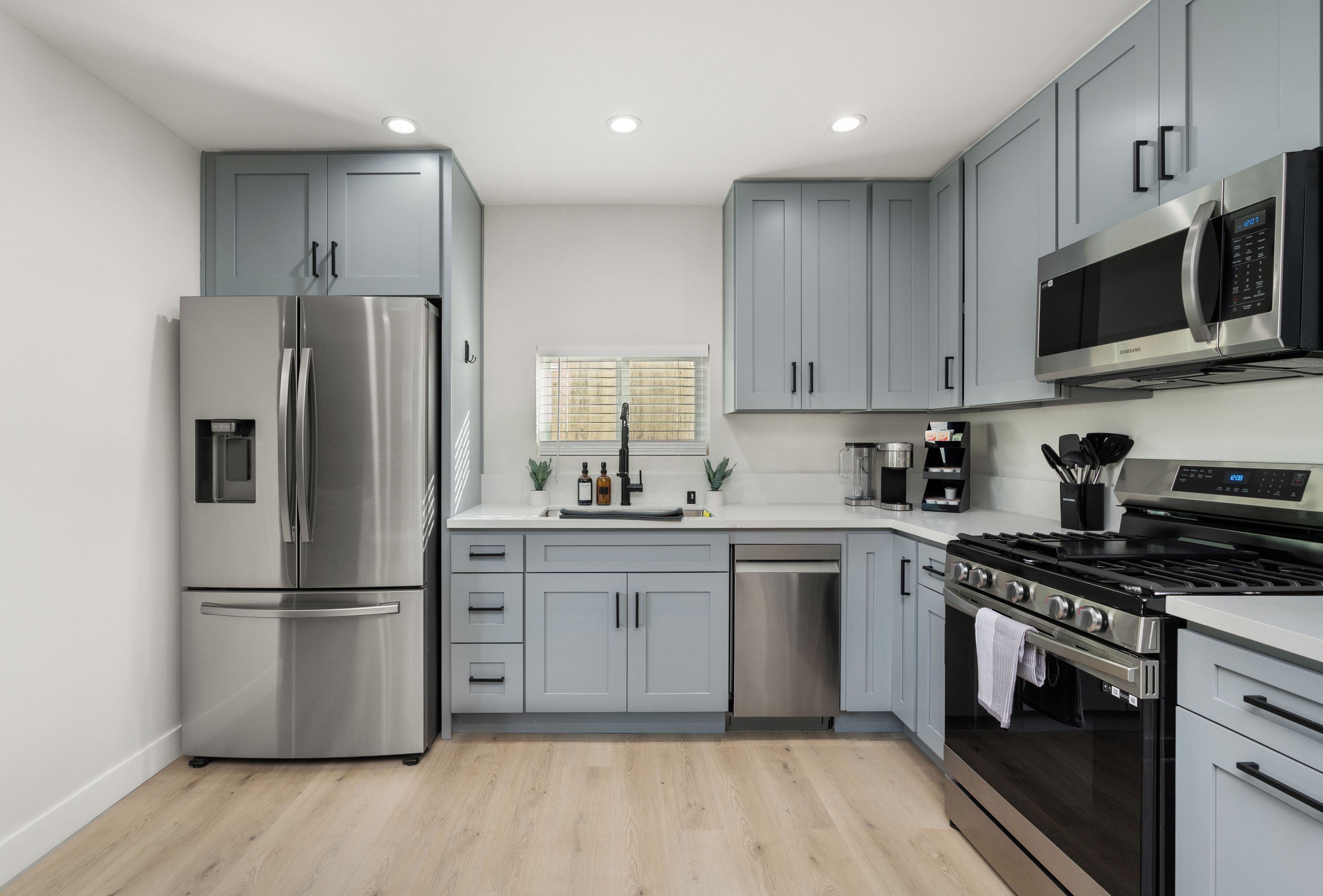 Une cuisine moderne dotée d’appareils électroménagers en acier inoxydable, de meubles de rangement gris et d’un plancher en bois.