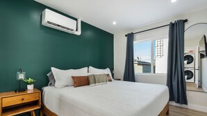 Een slaapkamer met een bed, een nachtkastje, een lamp, een bloempot en uitzicht op een wasruimte.