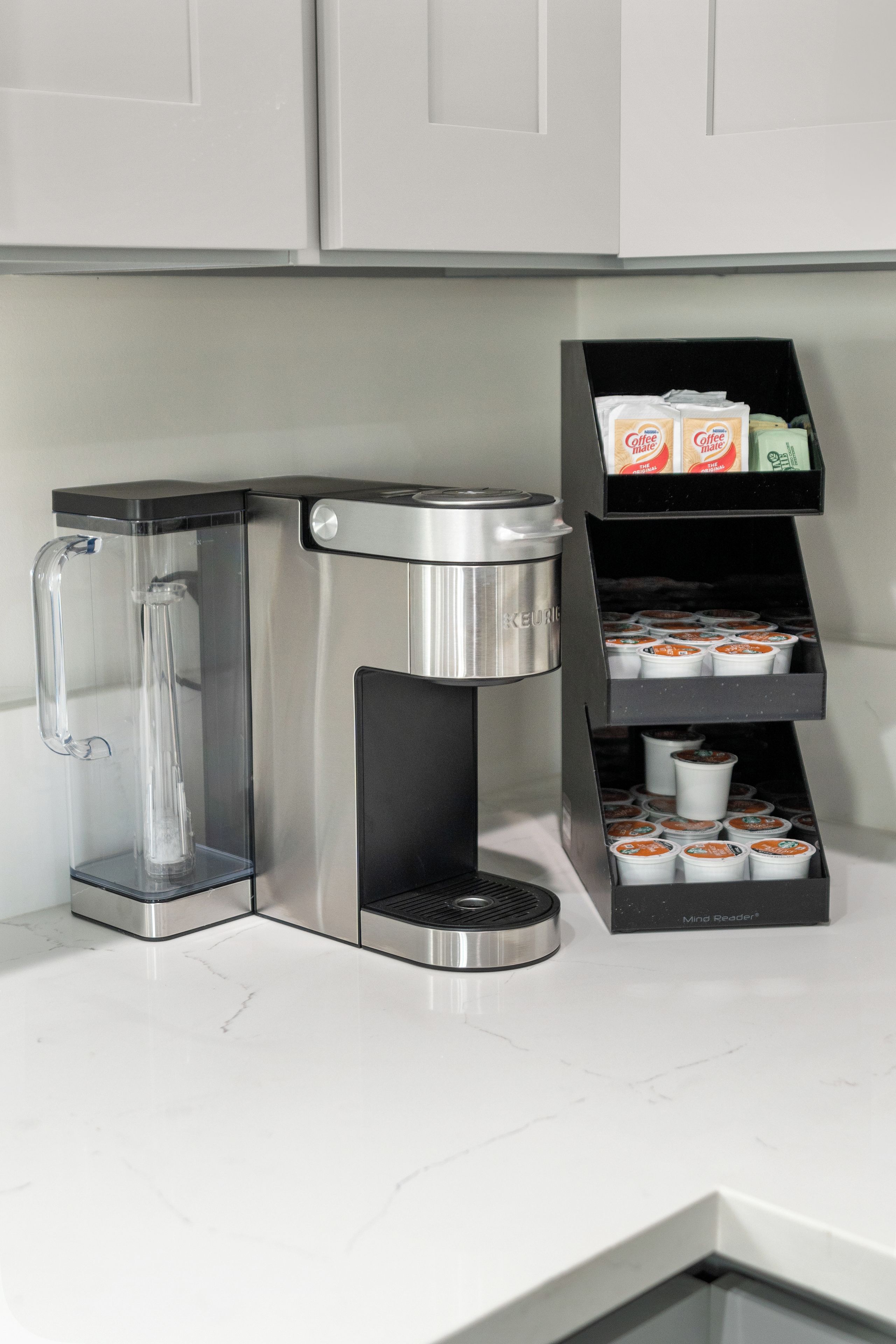 Une machine à café dotée d’un réservoir d’eau et d’un bac de récupération, placée à côté d’un distributeur de capsules de café contenant plusieurs capsules.