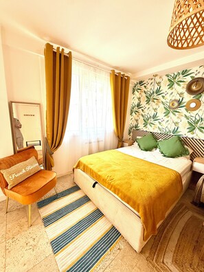 A hotel room with a bed, a chair, a window with curtains, a wall with a floral pattern, and a hanging light fixture. - Stylish Studio in the Heart of Cannes – Central Location & Contemporary Comfort” (Cannes)