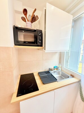 A compact kitchen with a built-in microwave, a stovetop, and a sink. - Stylish Studio in the Heart of Cannes – Central Location & Contemporary Comfort” (Cannes)