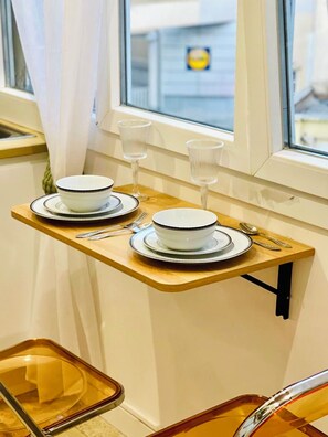 A dining area with a window view, a wooden table with plates and cutlery, and a glass tray. - Stylish Studio in the Heart of Cannes – Central Location & Contemporary Comfort” (Cannes)