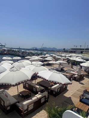 A beachside area with multiple white umbrellas, lounge chairs, and tables arranged for outdoor seating. - Stylish Studio in the Heart of Cannes – Central Location & Contemporary Comfort” (Cannes)