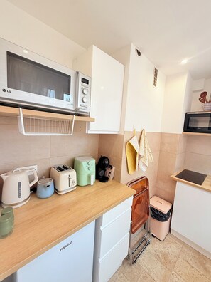 A compact kitchen with a microwave, toaster, kettle, and a small air fryer on the counter. - Stylish Studio in the Heart of Cannes – Central Location & Contemporary Comfort” (Cannes)